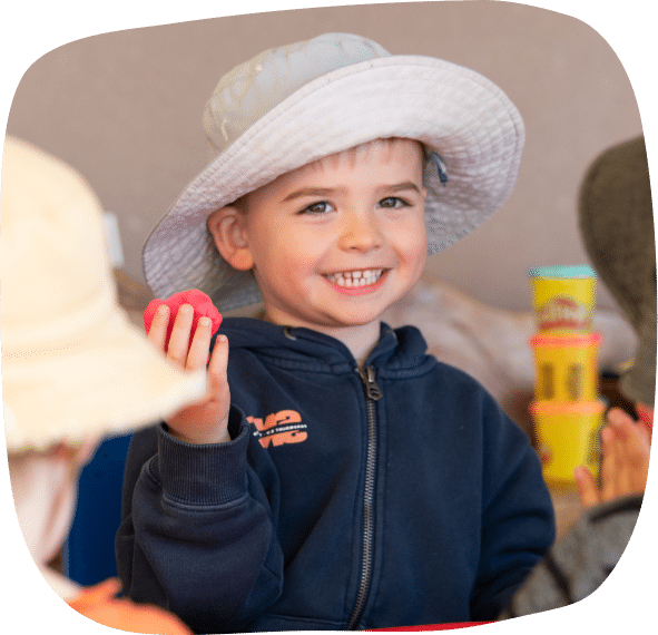 Smiling child holding pink clay at preschool